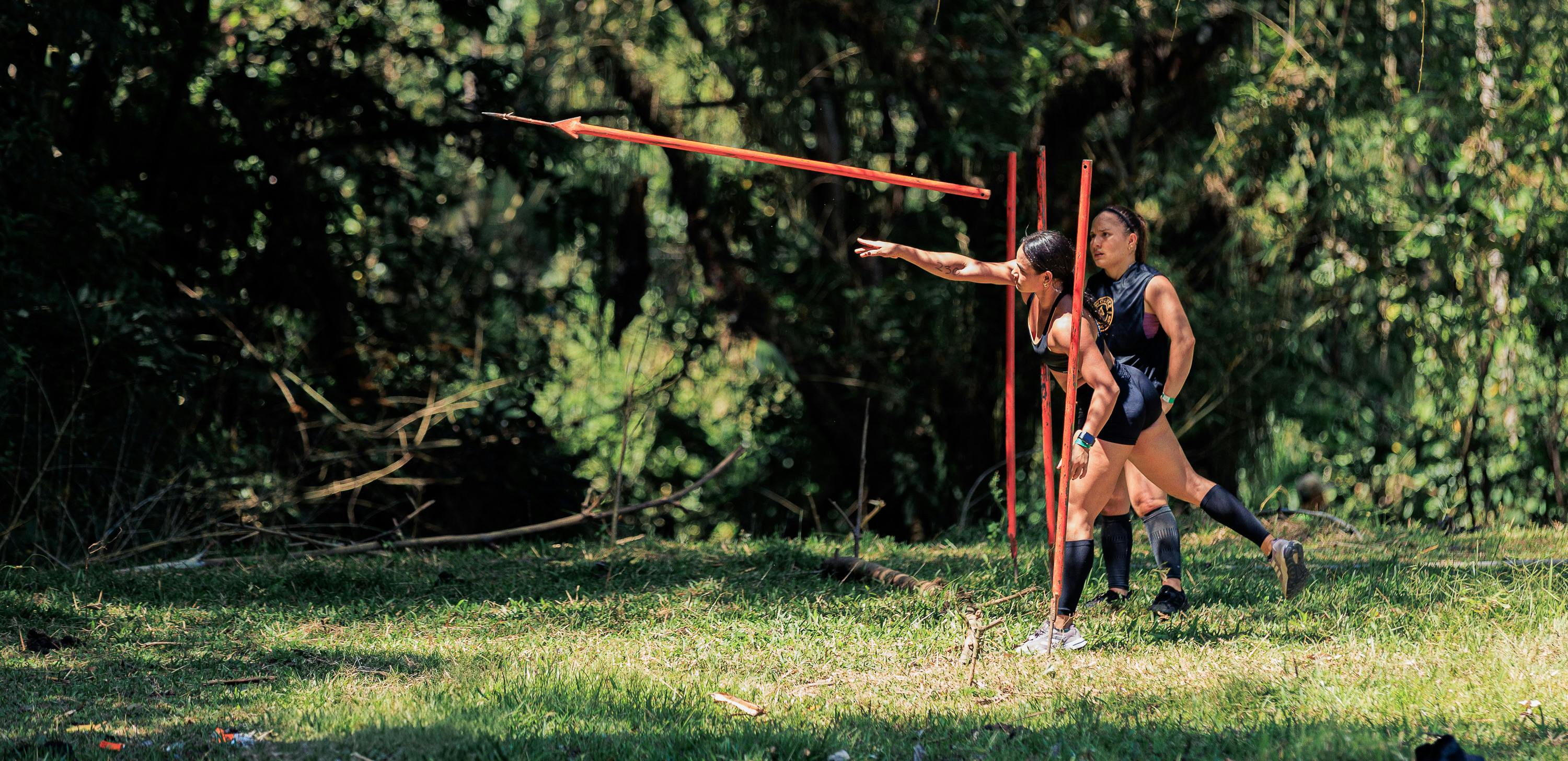Two women practicing javelin throw outdoors in a lush forest setting in Colombia.