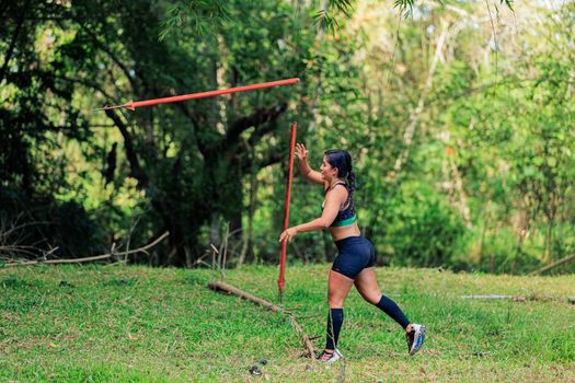 Athletic woman practicing javelin throw in a vibrant green forest setting during daytime. — photo by CRISTIAN CAMILO  ESTRADA
