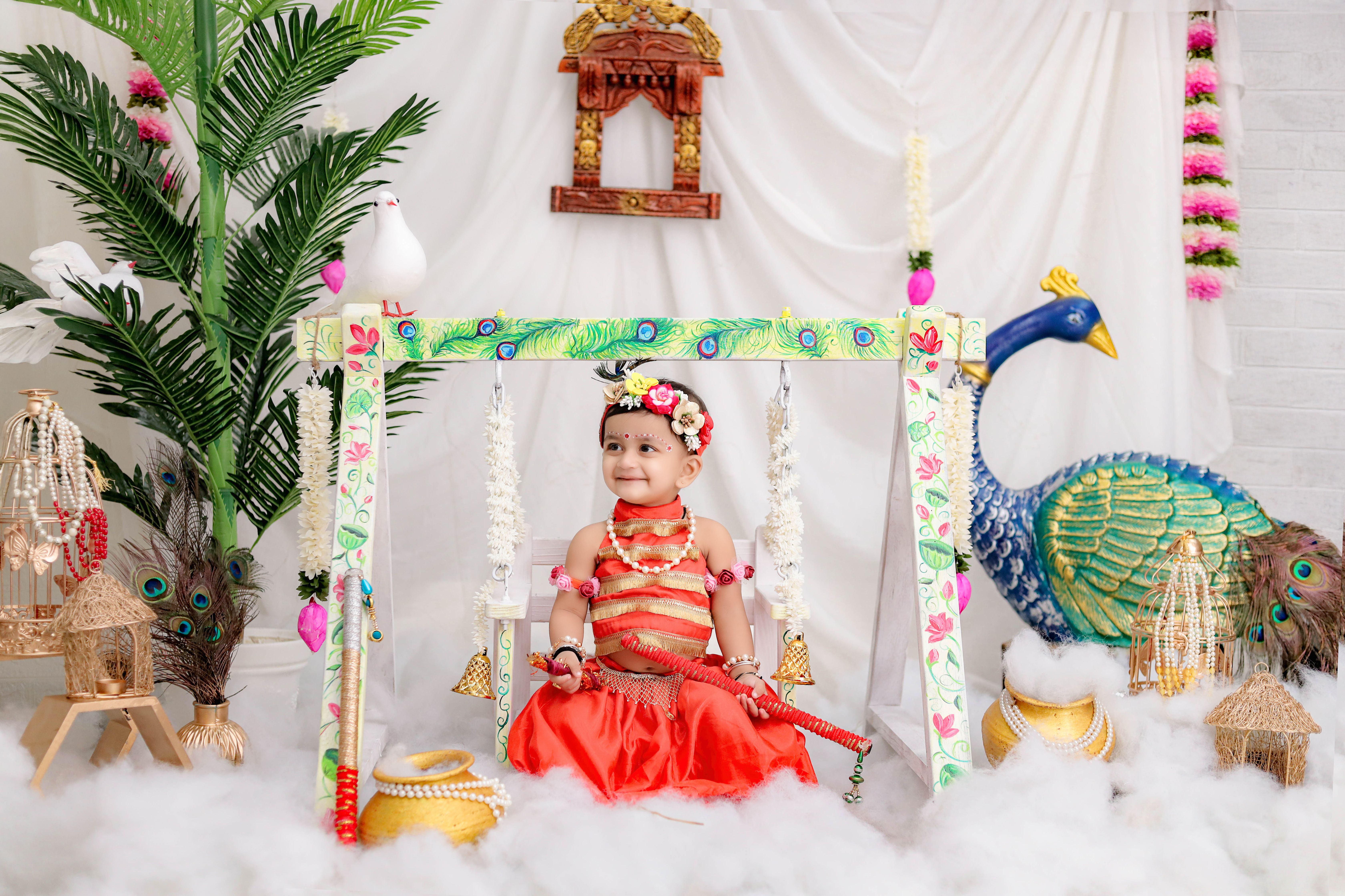 Charming baby dressed in vibrant Indian attire sits on a decorative swing with festive ornaments.