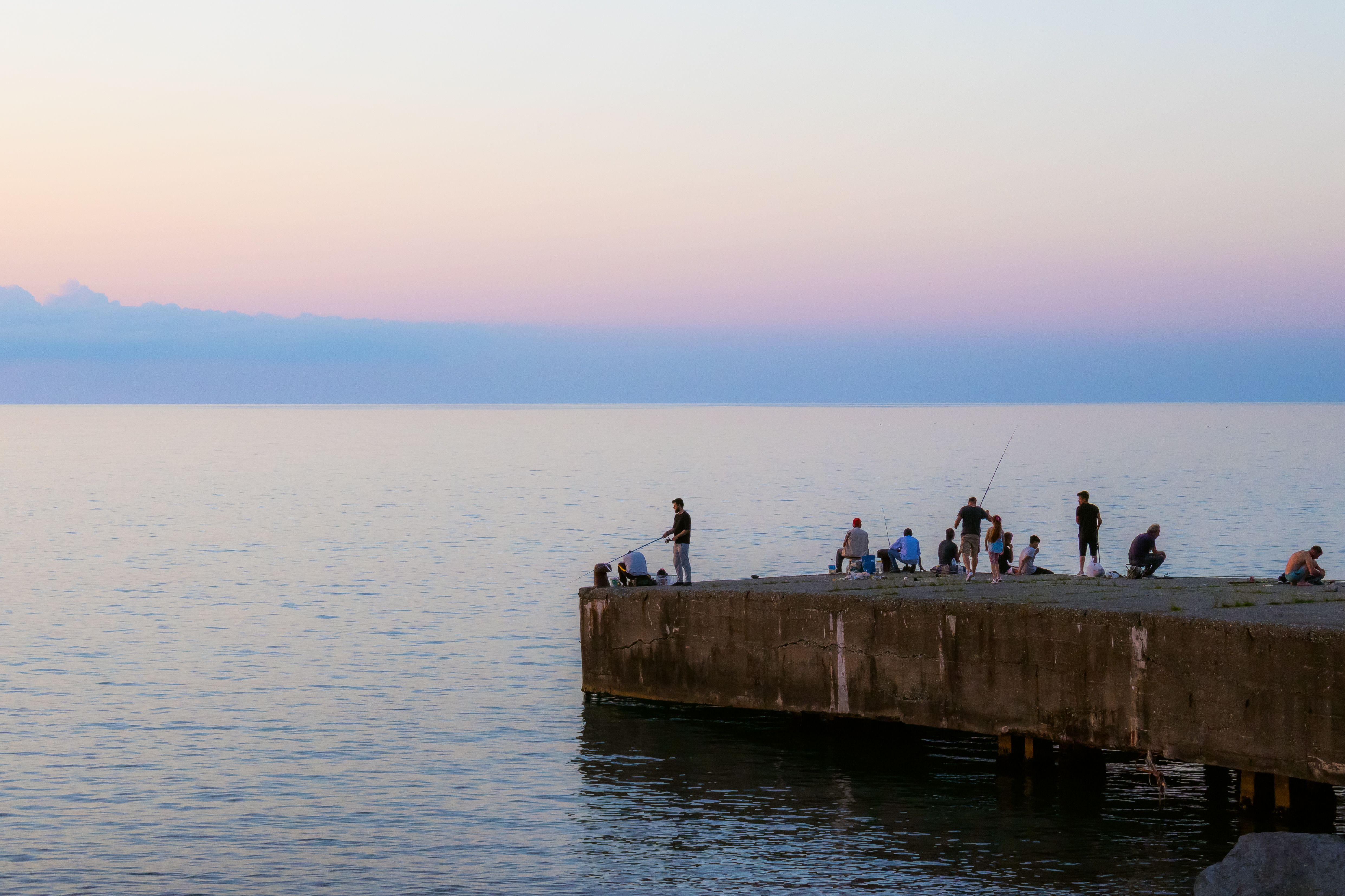 Silhouetted fishermen enjoy a tranquil evening on a jetty by the sea at sunset.