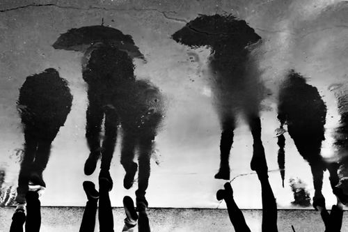 Free Silhouetted reflections of people with umbrellas during a rainy day on the street. Stock Photo