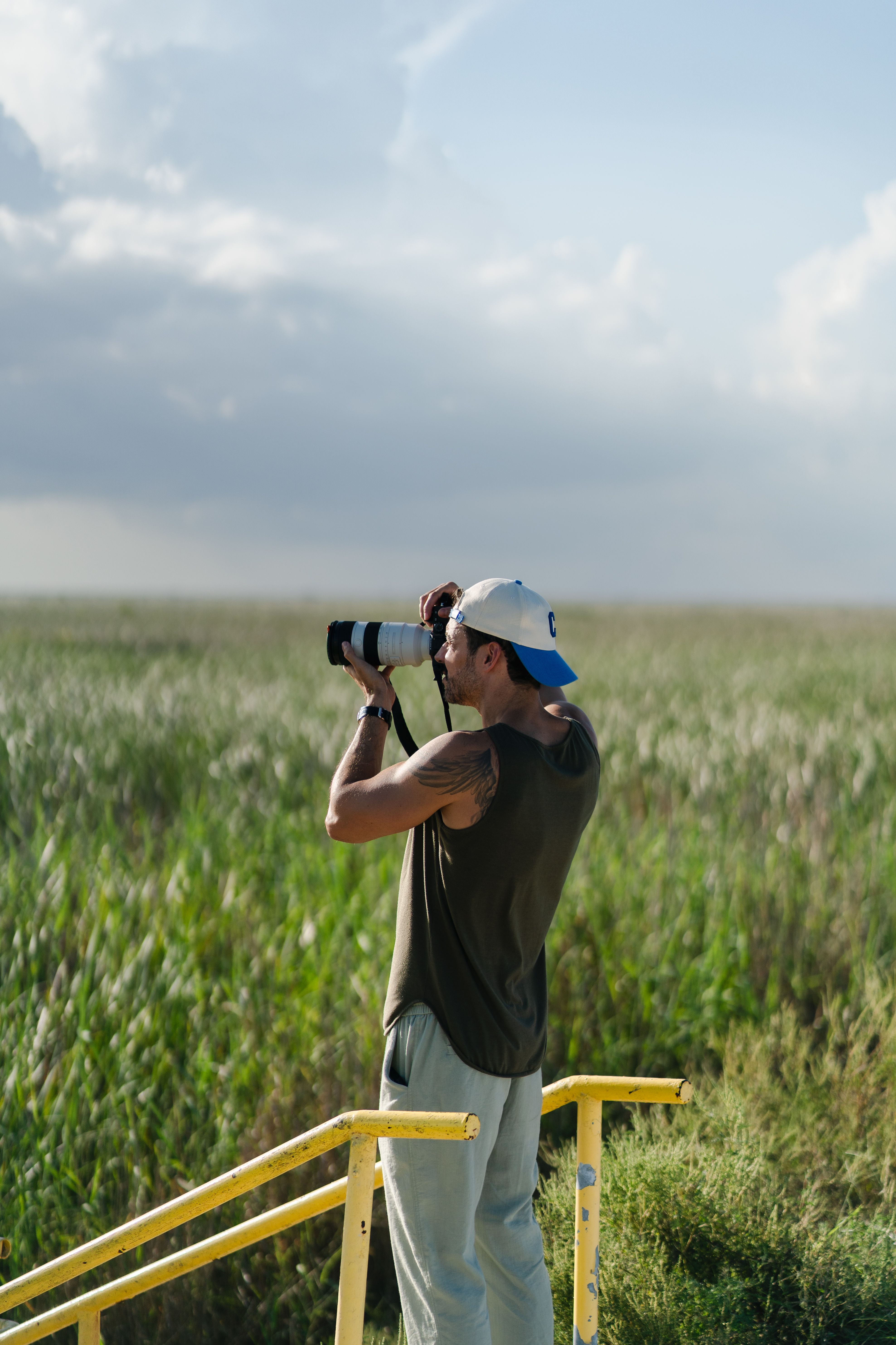 A photographer with a cap captures the scenic field in daylight.