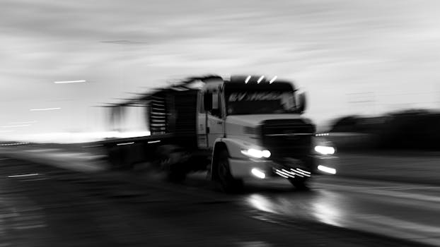 Dynamic black and white photo depicting a moving truck on a rainy road, creating a dramatic blur effect.