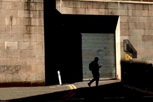 Free A silhouette of a person walking under the interplay of light and shadow on an urban street. Stock Photo