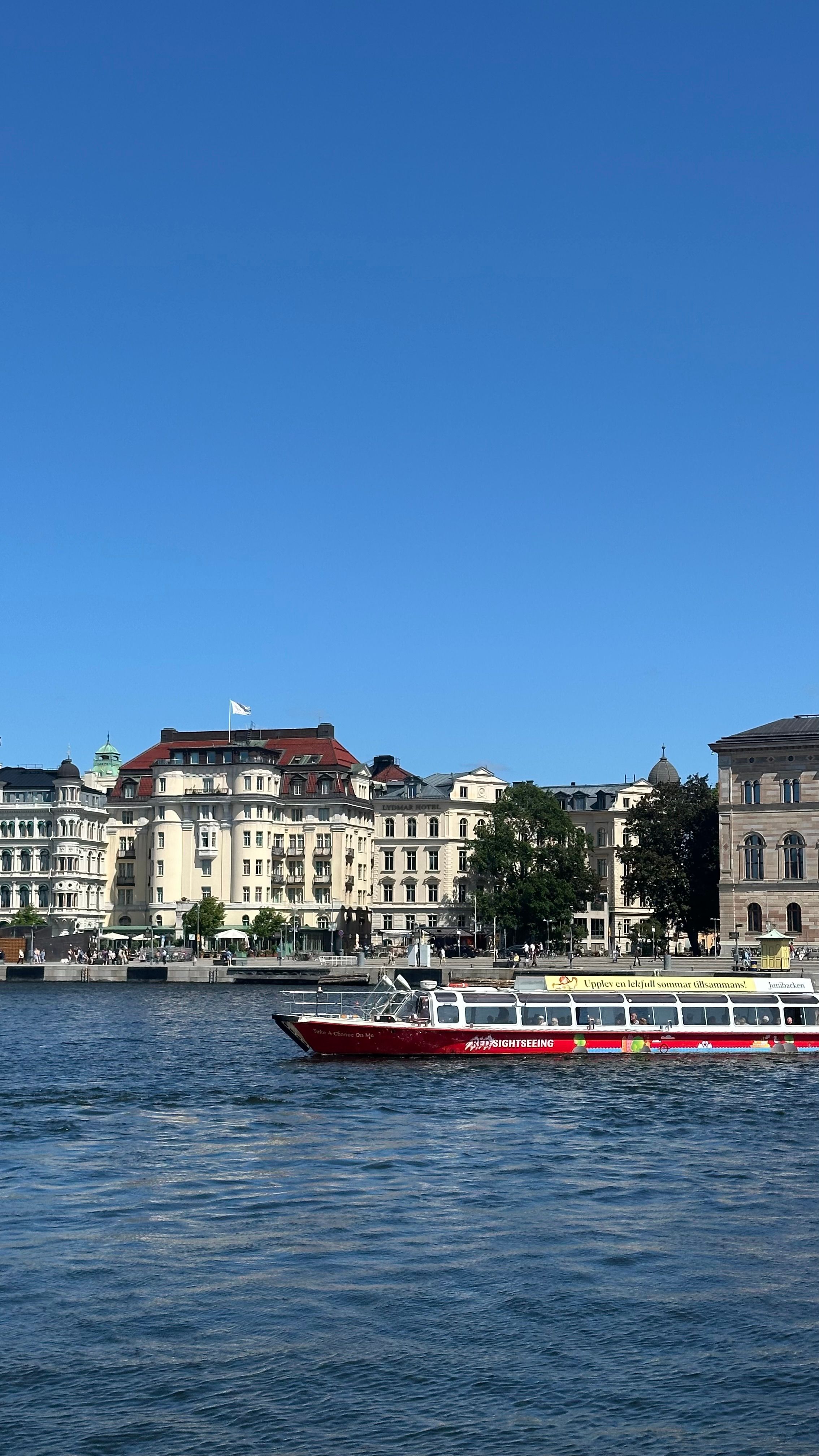 Gratis En turbåt cruiser forbi historiske bygninger ved vannkanten i Stockholm på en solrik dag. Arkivbilde
