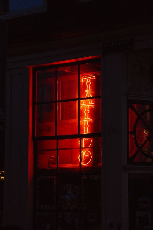 Free Moody neon 'Tattoo' sign glows in a dark Amsterdam window, showcasing urban nightlife. Stock Photo