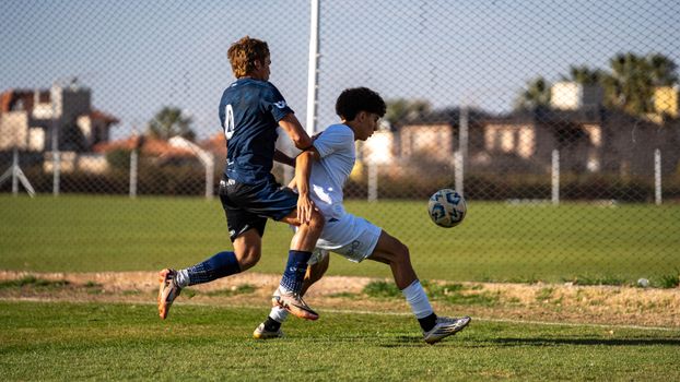 Two players competing in a heated soccer match outdoors on a sunny day.
