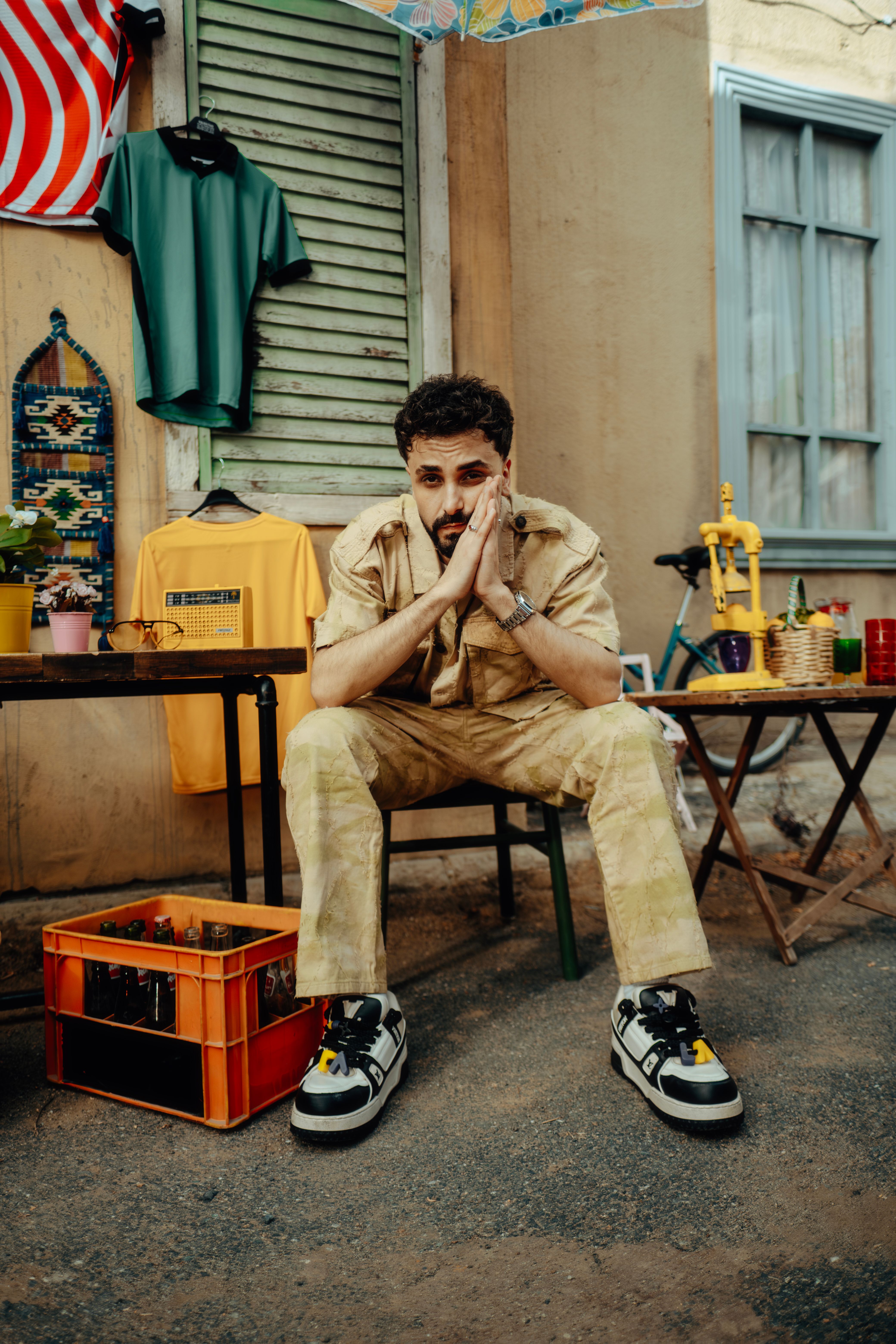 Man sitting on a chair in a casual outfit surrounded by urban street decor and colorful objects.