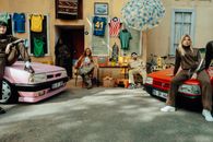 Vibrant street scene with diverse group posing by vintage cars in urban setting.
