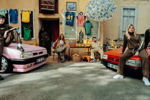 Vibrant street scene with diverse group posing by vintage cars in urban setting.