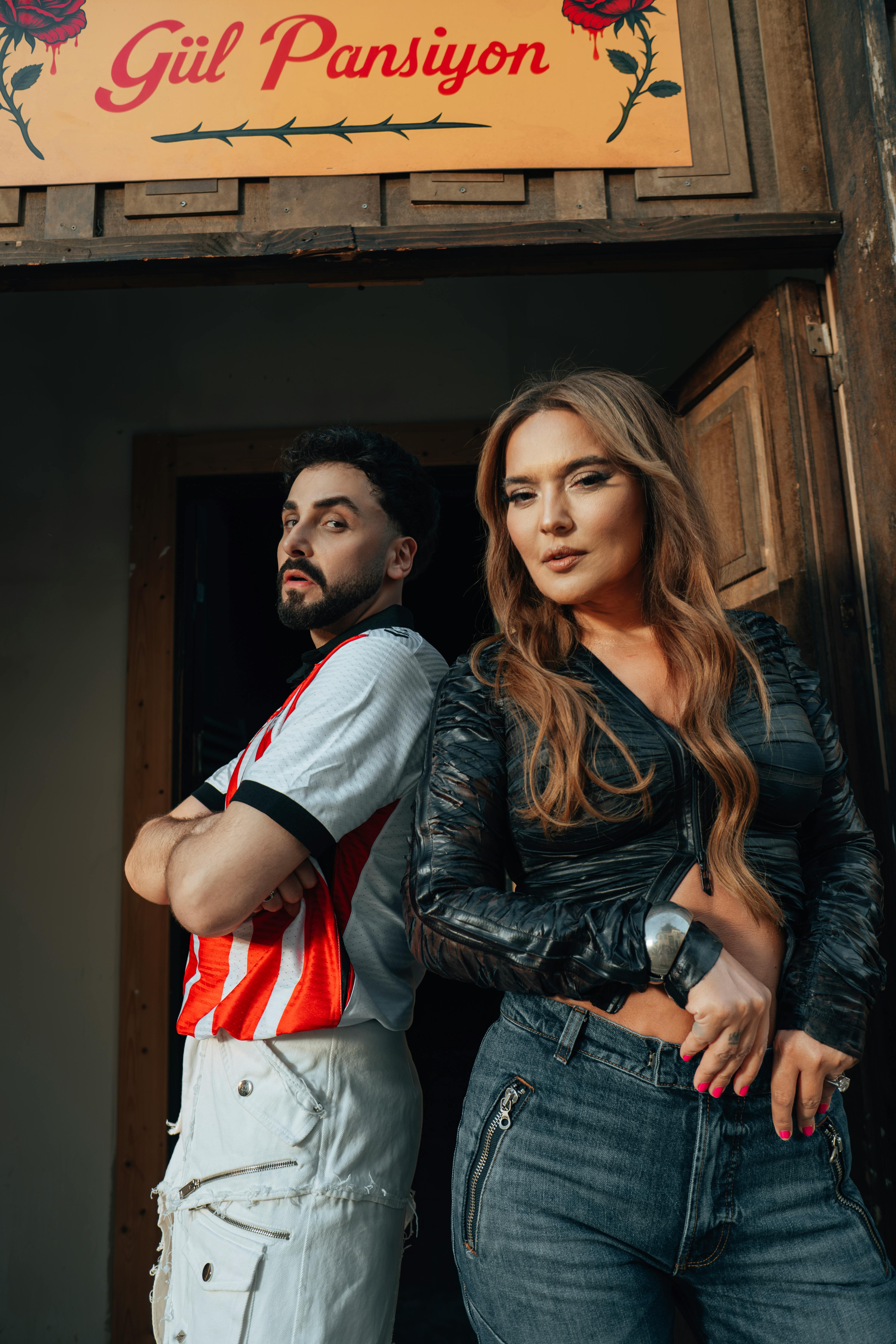 Two stylish adults striking dynamic poses in front of Güzel Pansiyon entrance.