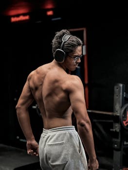 Focused male athlete wearing headphones, standing confidently in gym environment.