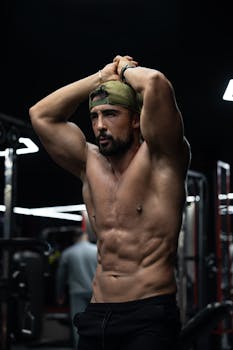 Athletic man in gym stretching arms, showcasing muscular build for fitness concept.