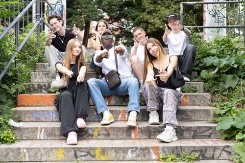 Free A diverse group of friends sitting on urban steps with graffiti, showing playful gestures. Stock Photo