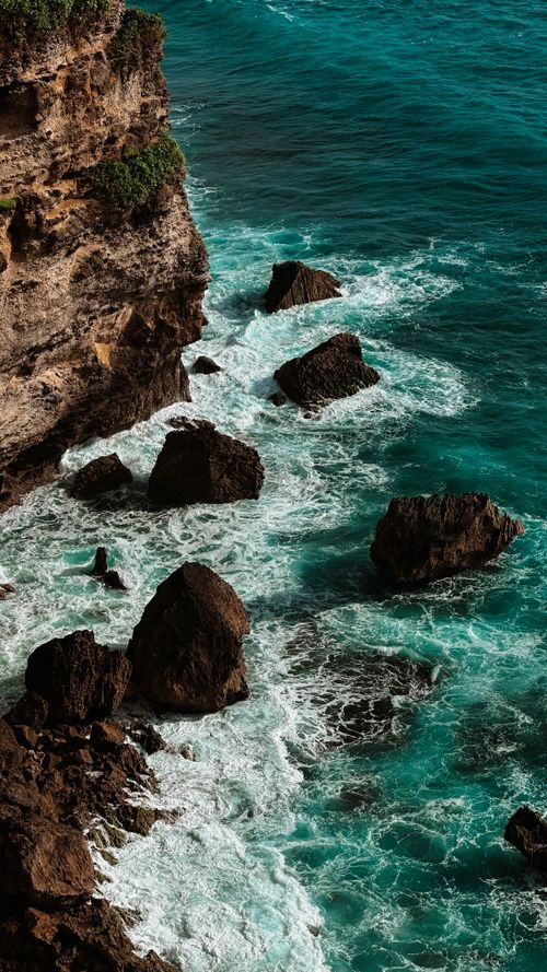 Free A breathtaking aerial view of ocean waves crashing against rocky cliffs on a sunny day. Stock Photo