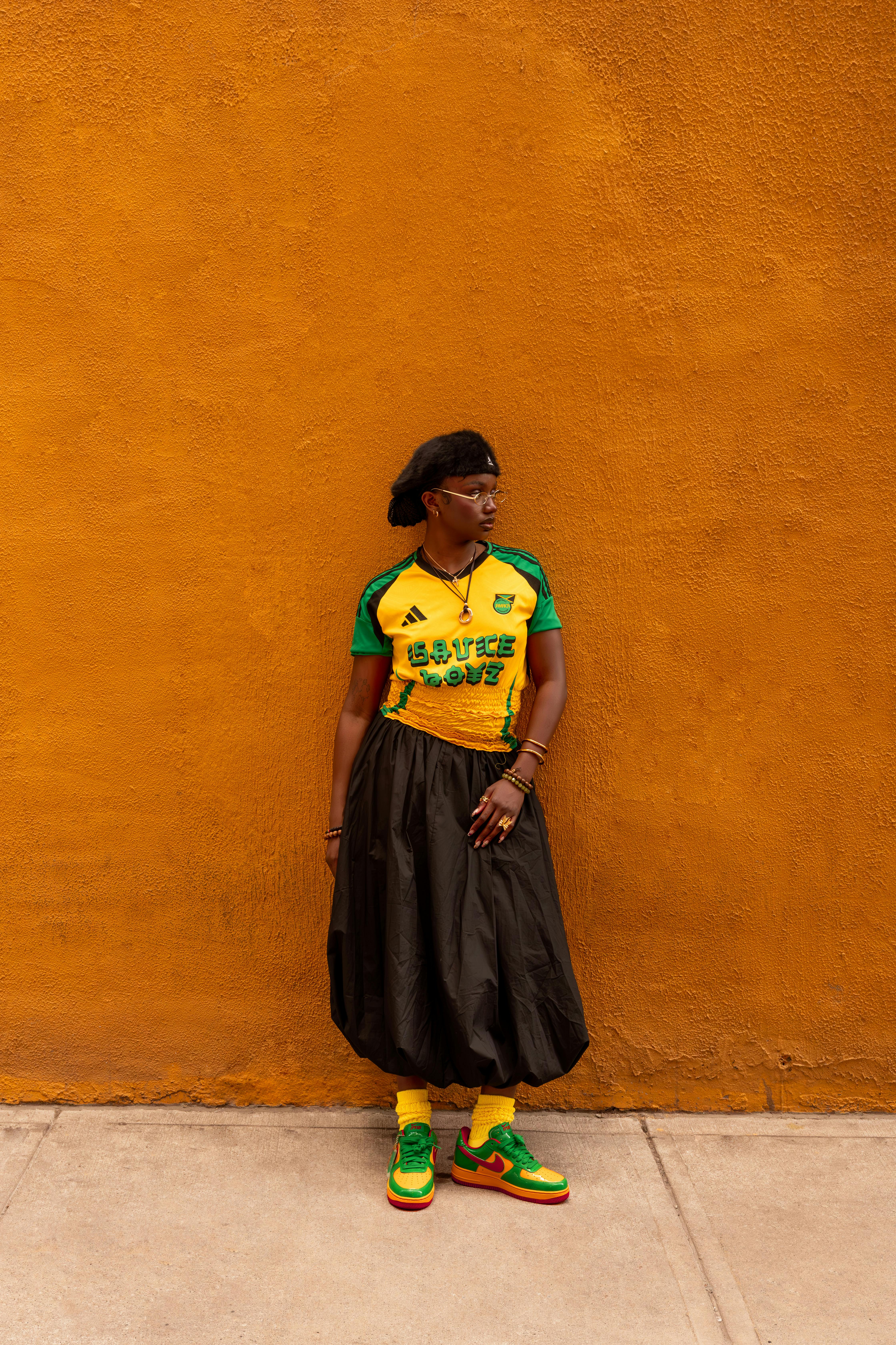 Fashionable adult in colorful attire posing against a vivid orange wall.