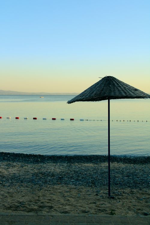 Free Serene sunrise at a calm beach with a lone umbrella on a sandy shore. Stock Photo