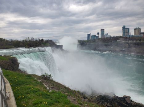 Stunning photo of Niagara Falls with mist and city skyline under cloudy sky.