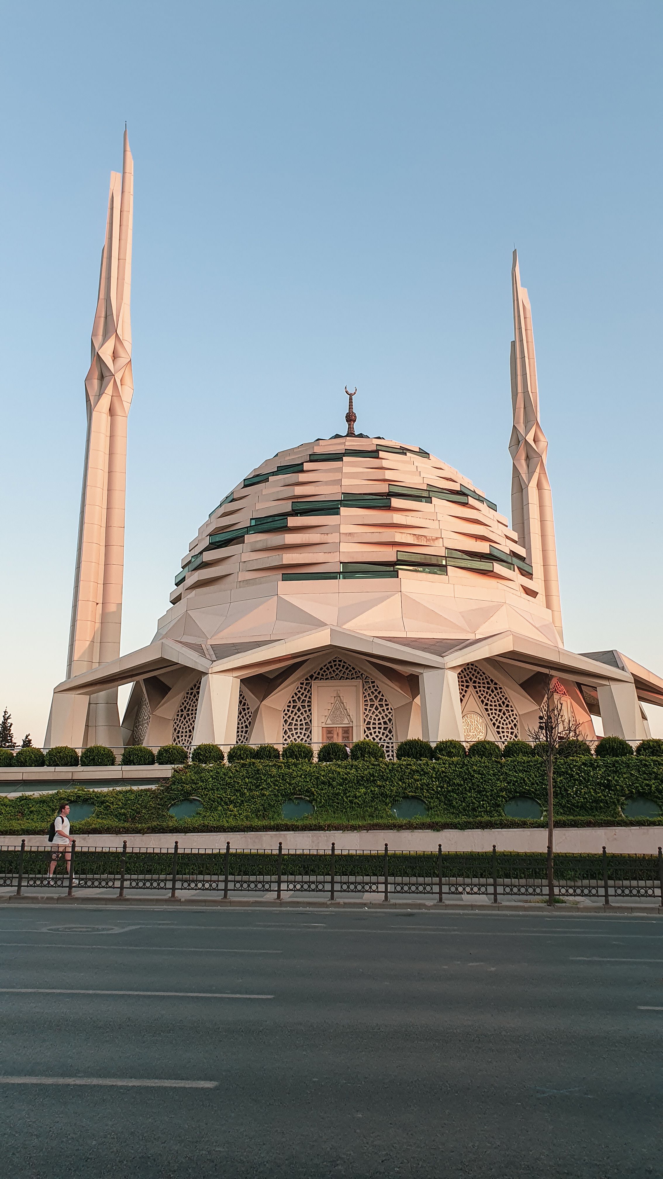 A striking modern mosque with geometric design and minarets against a sunset sky.