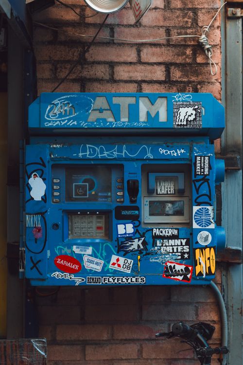 Free Colorful New York ATM adorned with diverse stickers against a brick wall, showcasing urban street art. Stock Photo