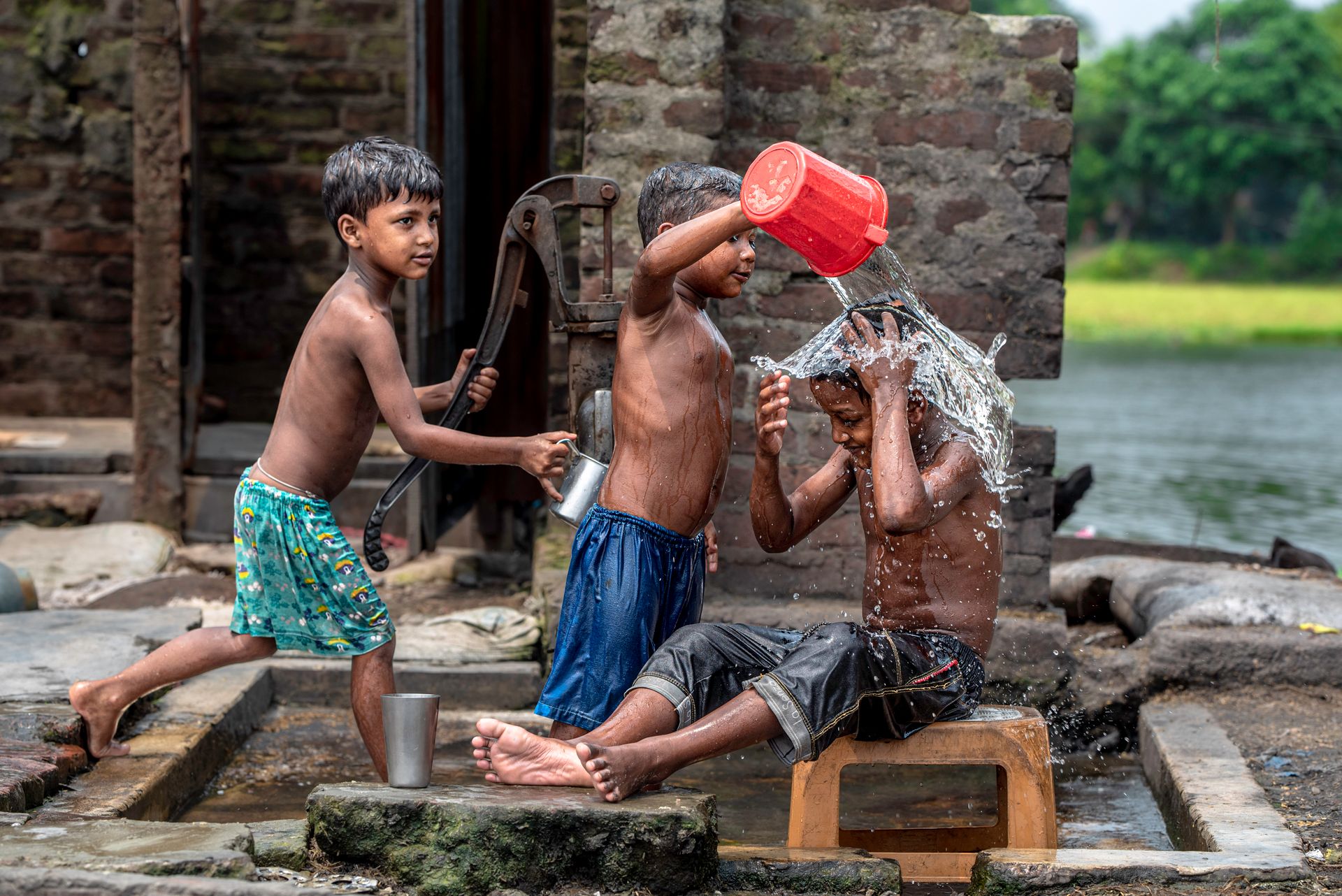 Three young boys joyfully playing with water near a pump outdoors, embodying summer fun.