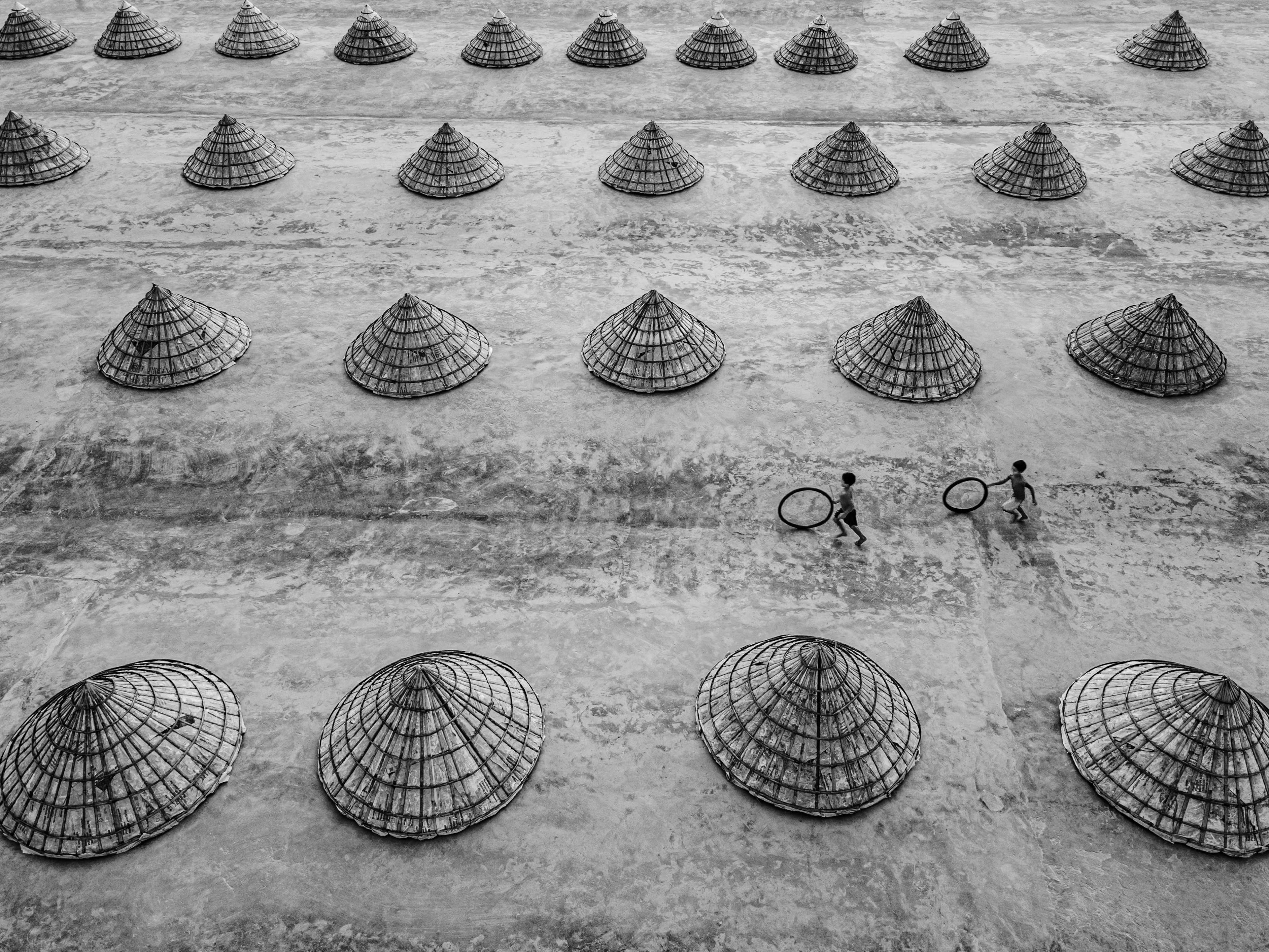Two children running with hoops among rows of basket covers in a symmetrical pattern.