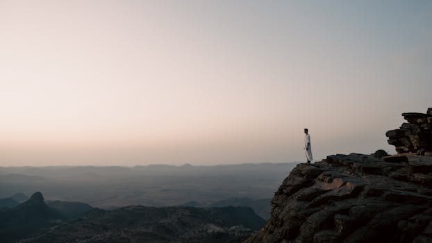 A person stands on a cliff in Tiznit, Morocco, overlooking a vast landscape at sunset.