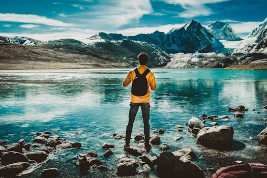 A man with a backpack stands by a serene mountain lake, reflecting the peaceful scenery.