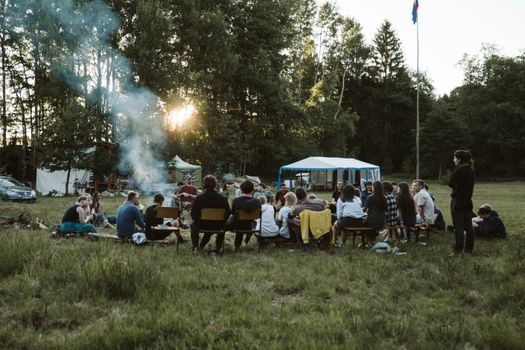 A group of adults relaxing around a campfire in a scenic outdoor setting with tents. - Fotografer Sidoarjo