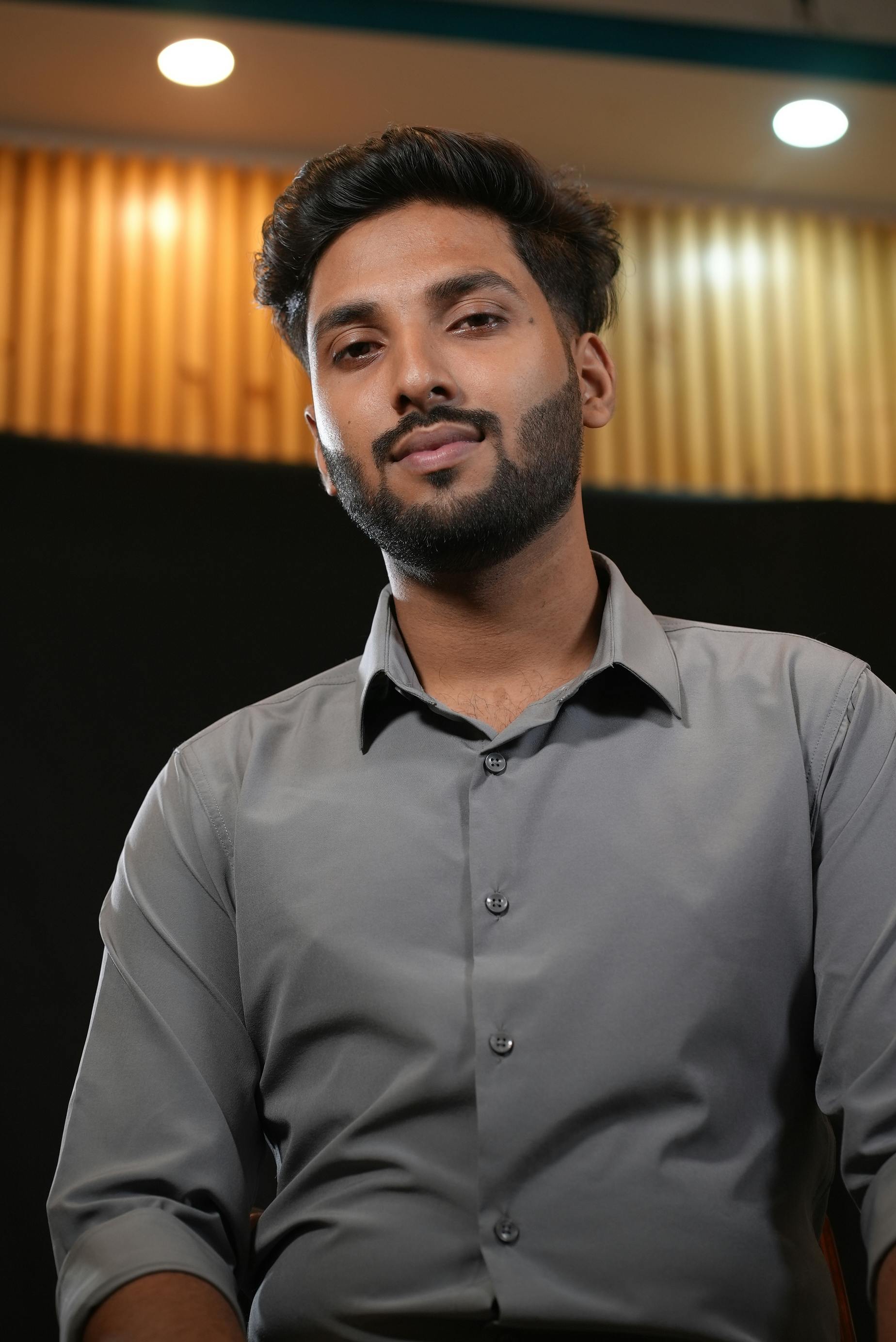 A young man in a grey shirt poses thoughtfully against a dark background with studio lighting.