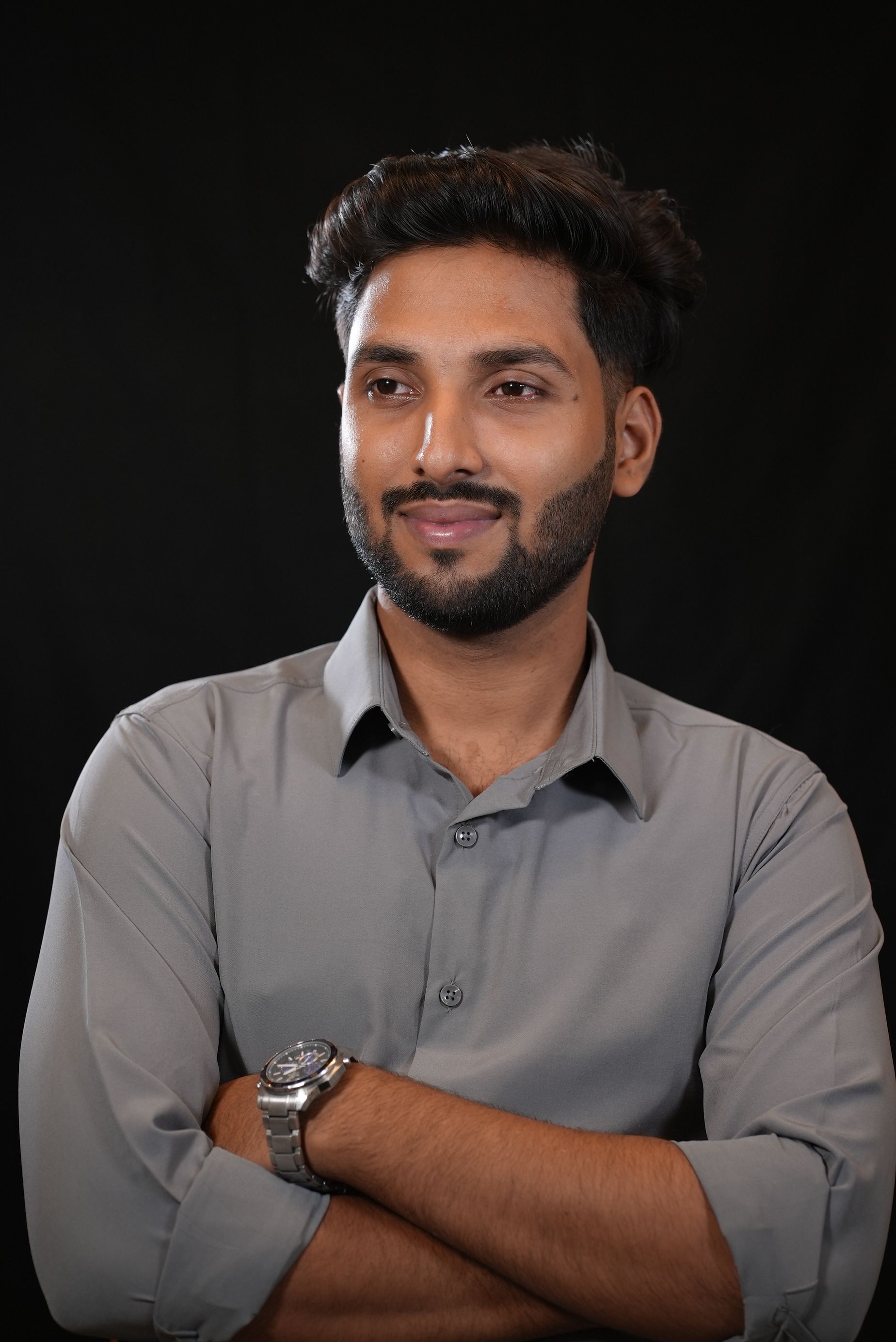 Stylish South Asian male posing confidently in a formal portrait with a dark background.