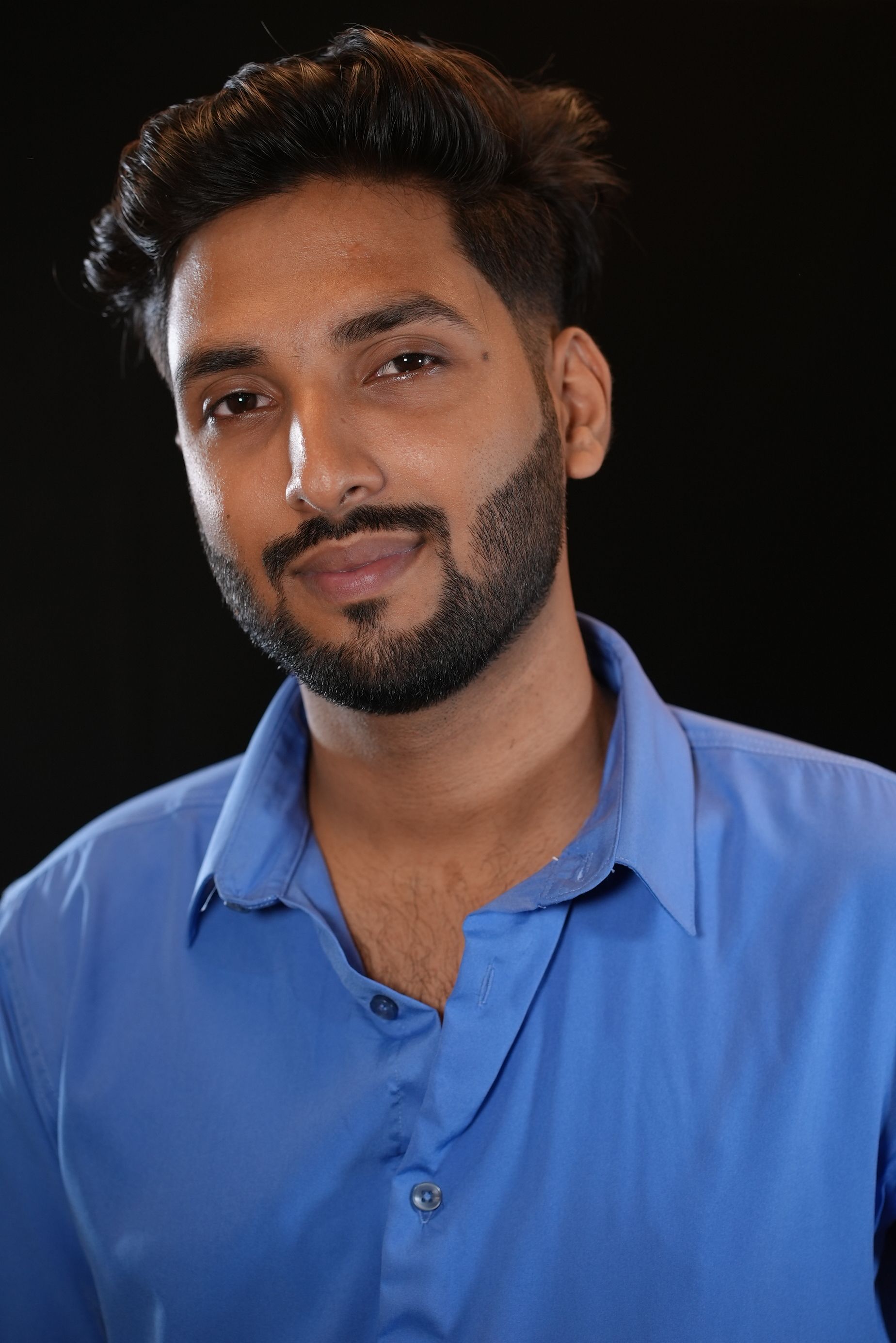 Studio portrait of a thoughtful young man in a blue shirt gazing confidently at the camera.