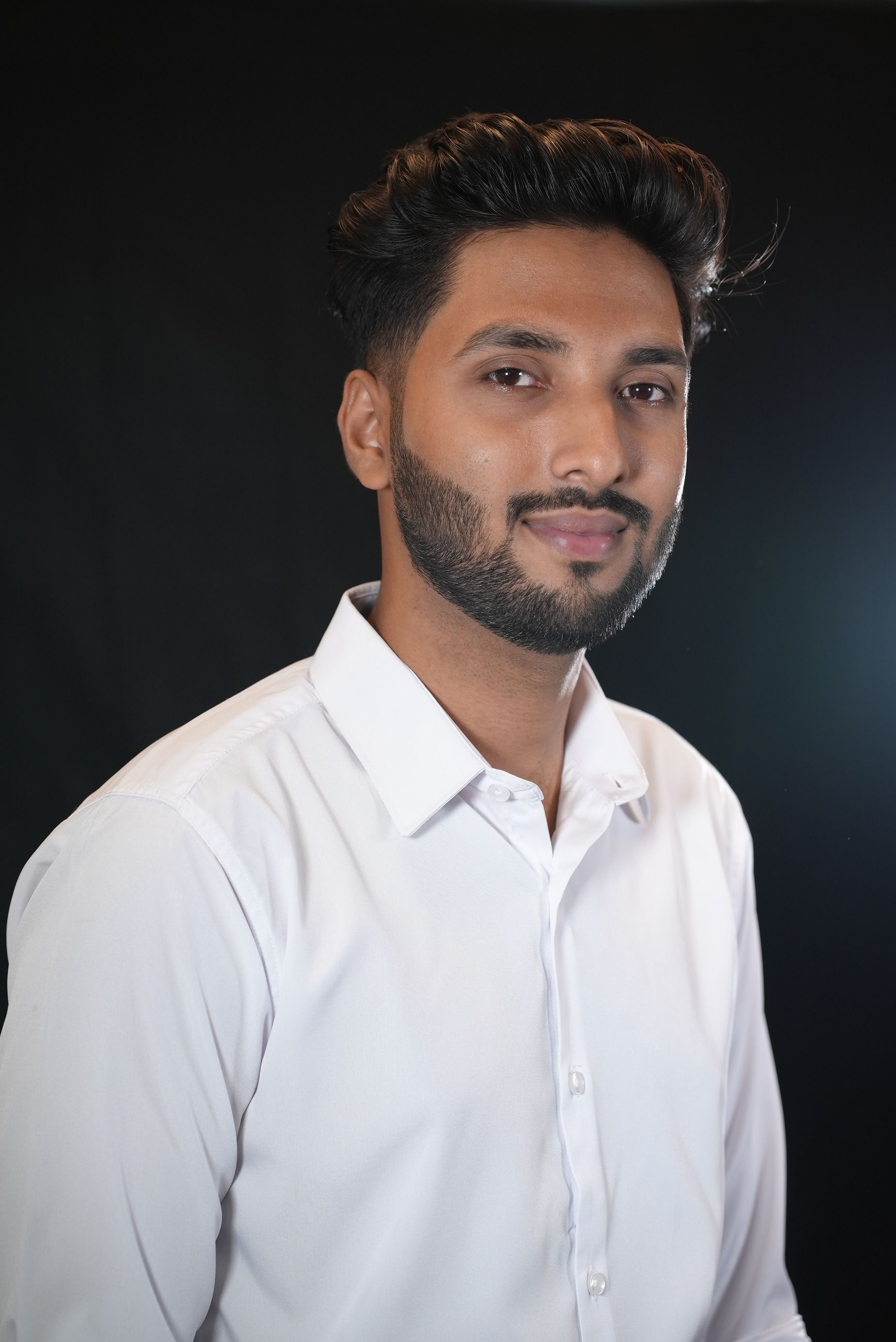 Studio portrait of a confident young man in white formal wear against a dark background.