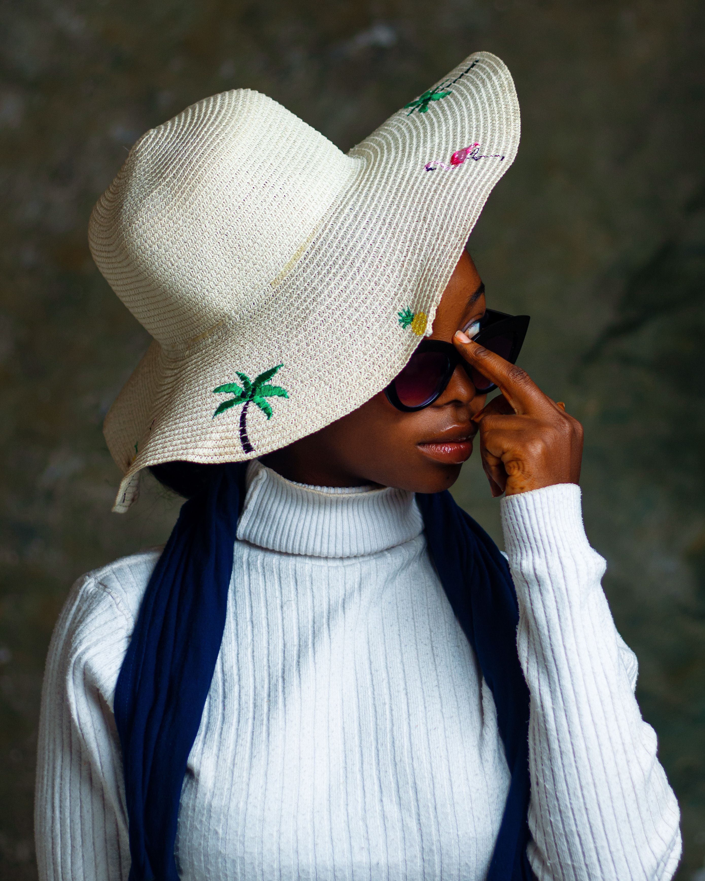 Elegant woman in a white sweater with a decorative sun hat adjusting sunglasses.
