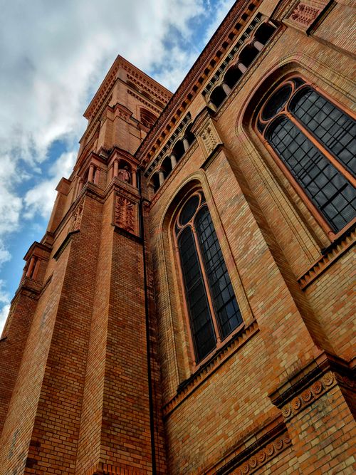 Free Close-up of a Gothic-style brick church facade reaching towards a partly cloudy sky. Stock Photo