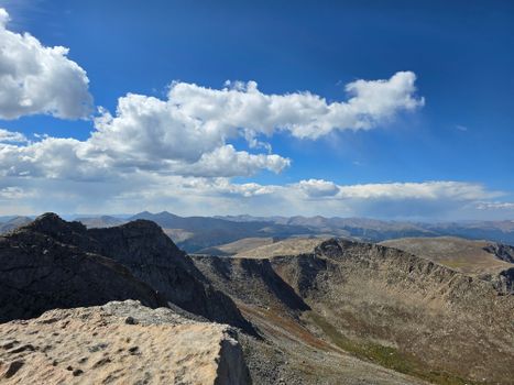 Expansive view of rugged mountain range with clear blue sky and fluffy clouds.