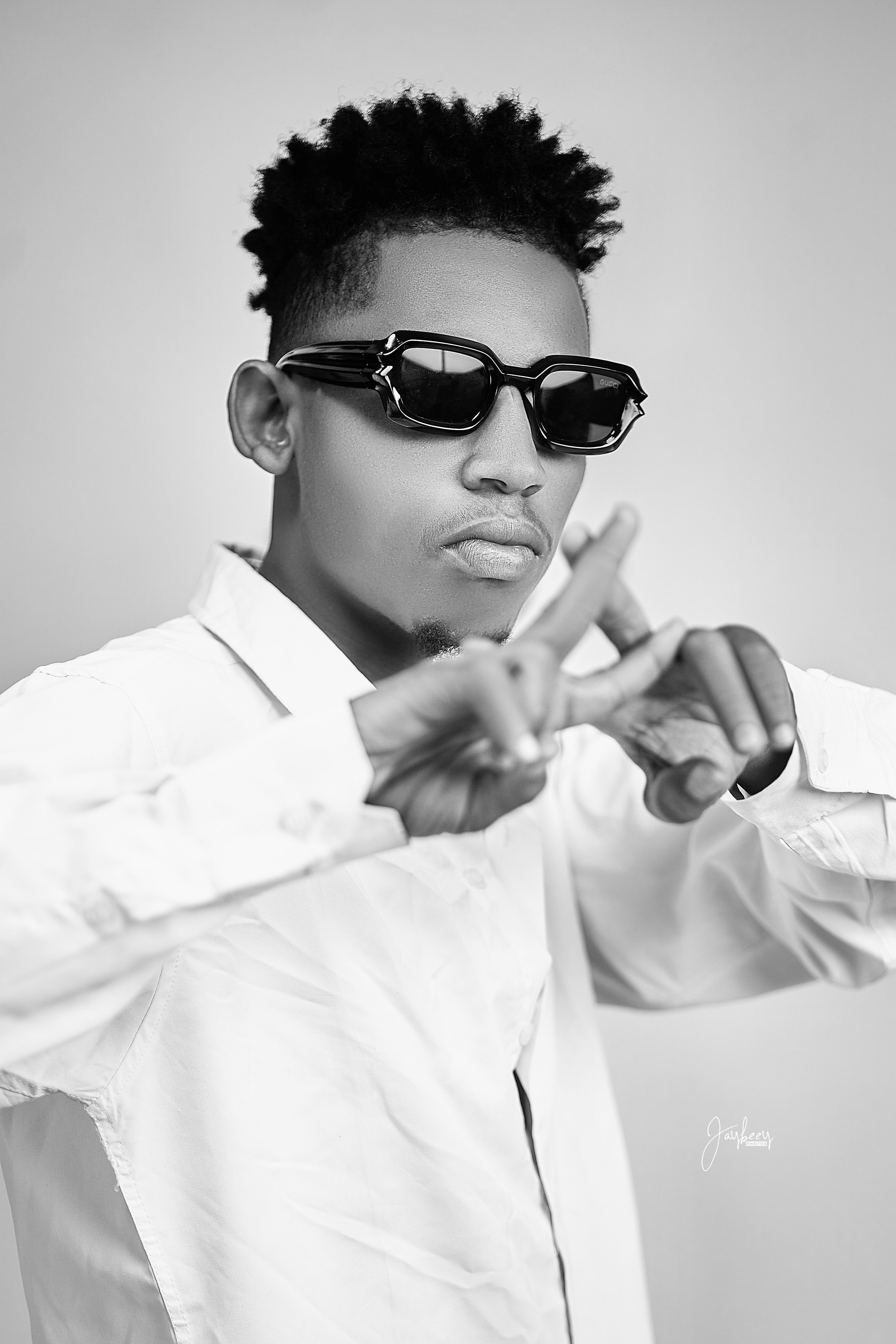 Black and white portrait of a stylish young Nigerian man wearing sunglasses making a trendy pose.