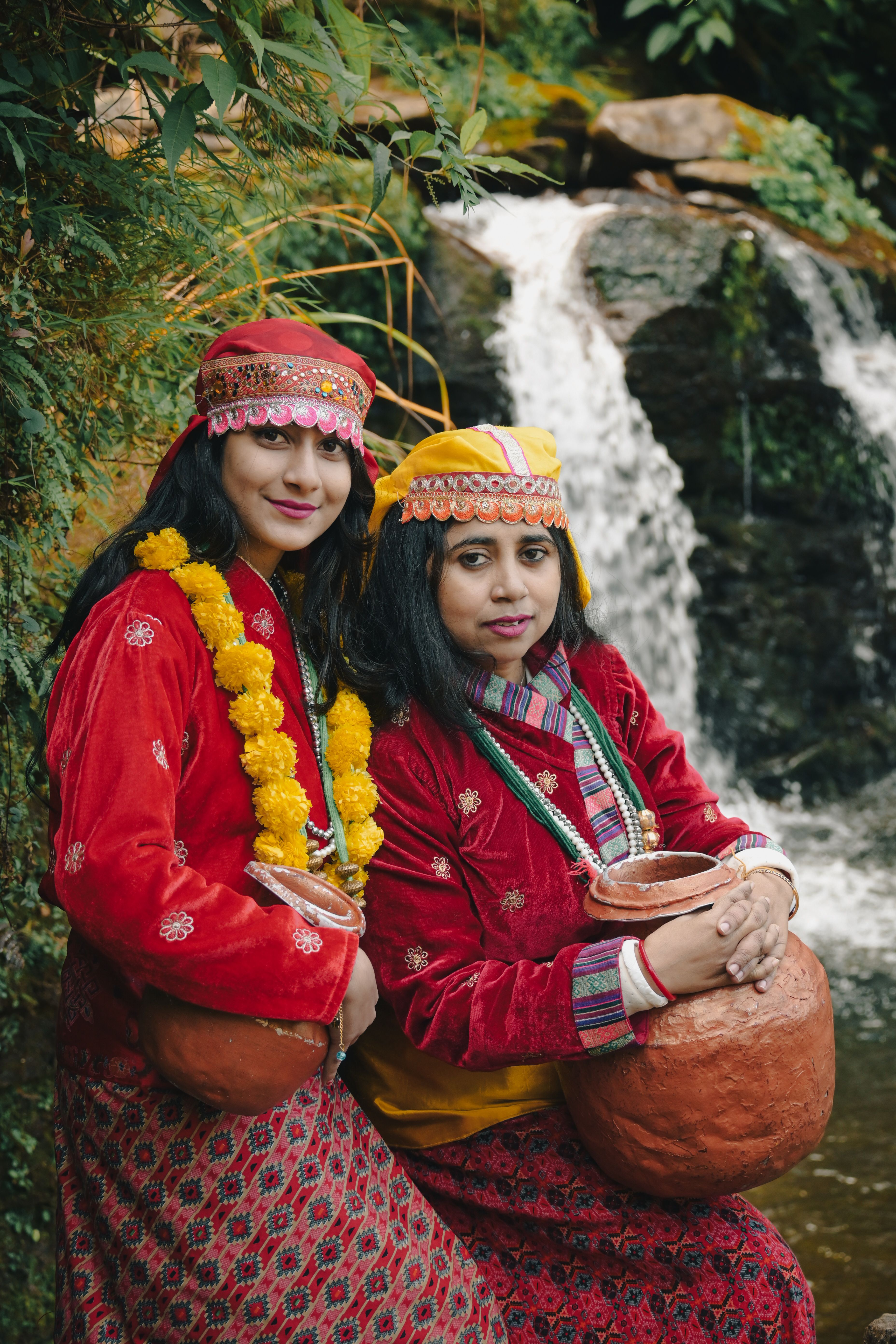 Two women in traditional attire by a waterfall in Darjeeling, India, showcasing cultural heritage.