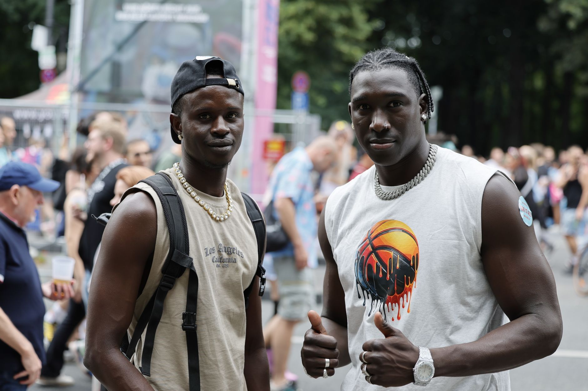 Two stylish men pose at a vibrant outdoor festival in Berlin, Germany.
