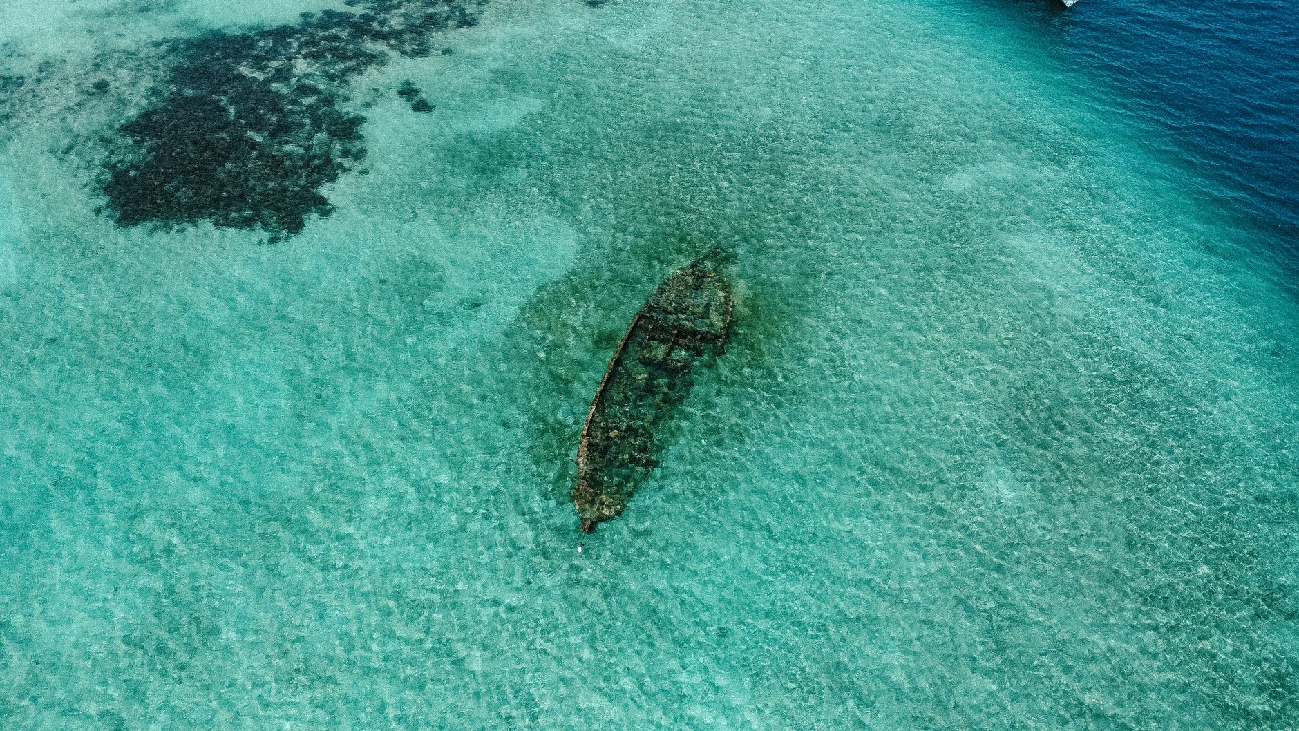 Aerial view captures a sunken ship in clear, turquoise waters, highlighting the ocean's beauty and mystery.