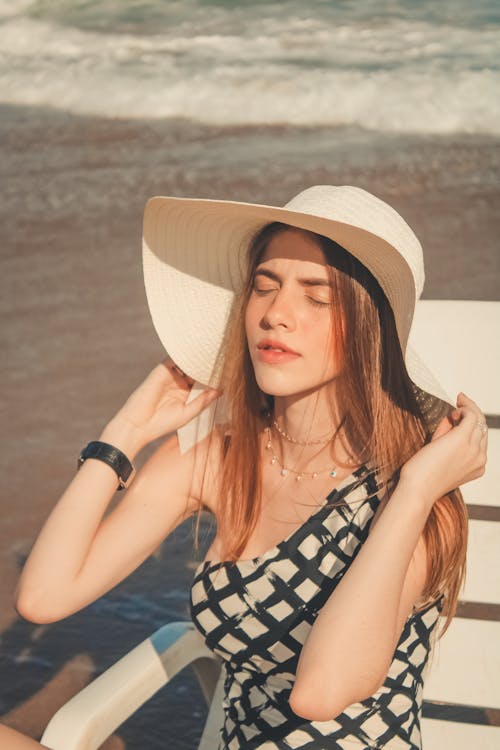 Photo of Woman Sitting on Sun Lounger While Holding Her Sun Hat