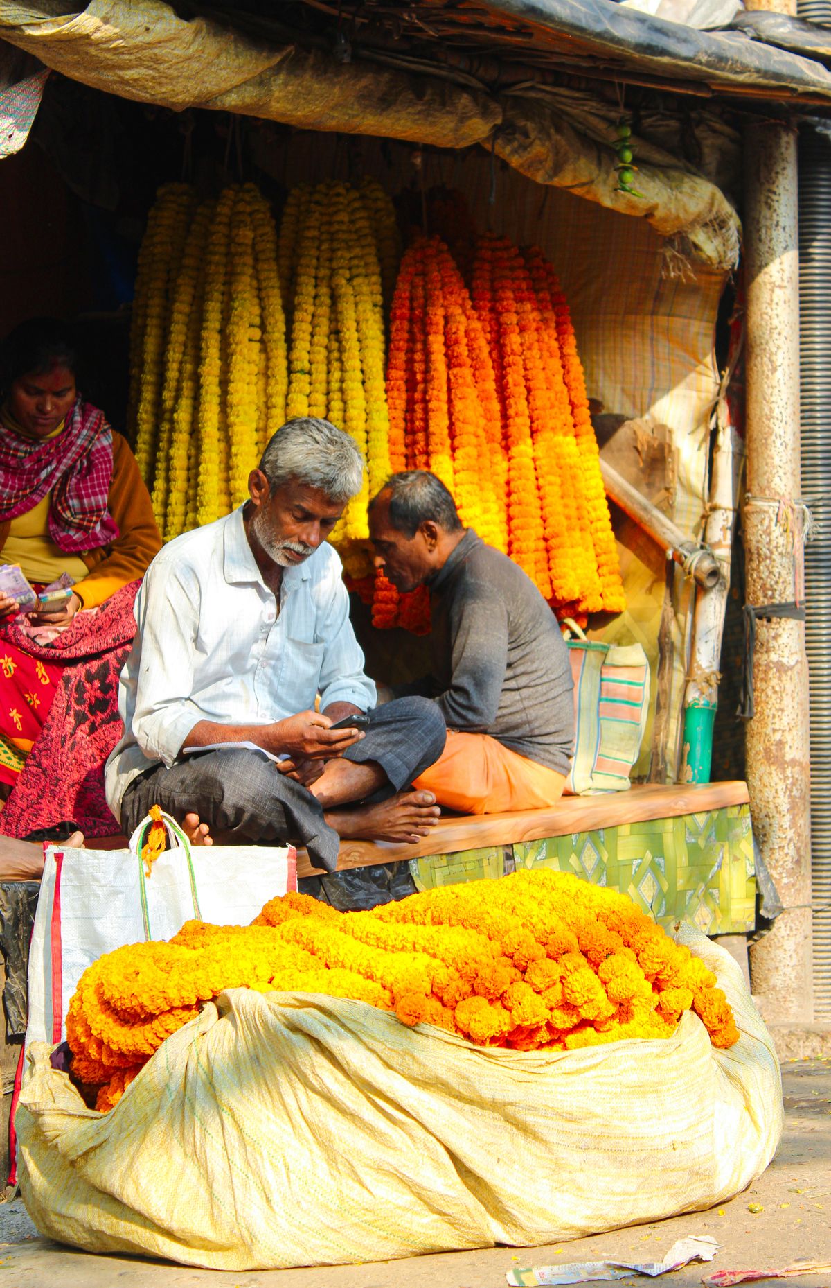 Marigold garlands hanging in long strings at an Indian flower market stall, sellers sitting under the awning