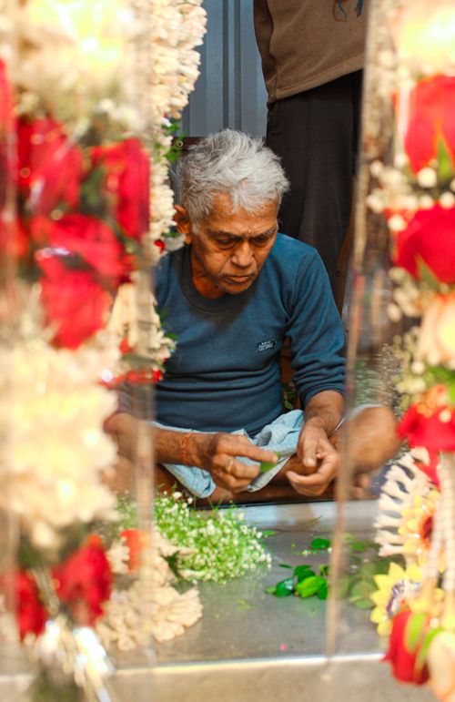 Free An elderly man skillfully makes flower garlands indoors with vibrant flowers. Stock Photo