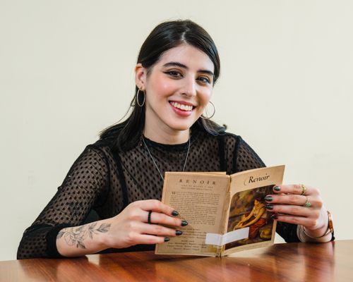 Free Young woman with tattoos reading a Renoir book indoors, smiling. Stock Photo