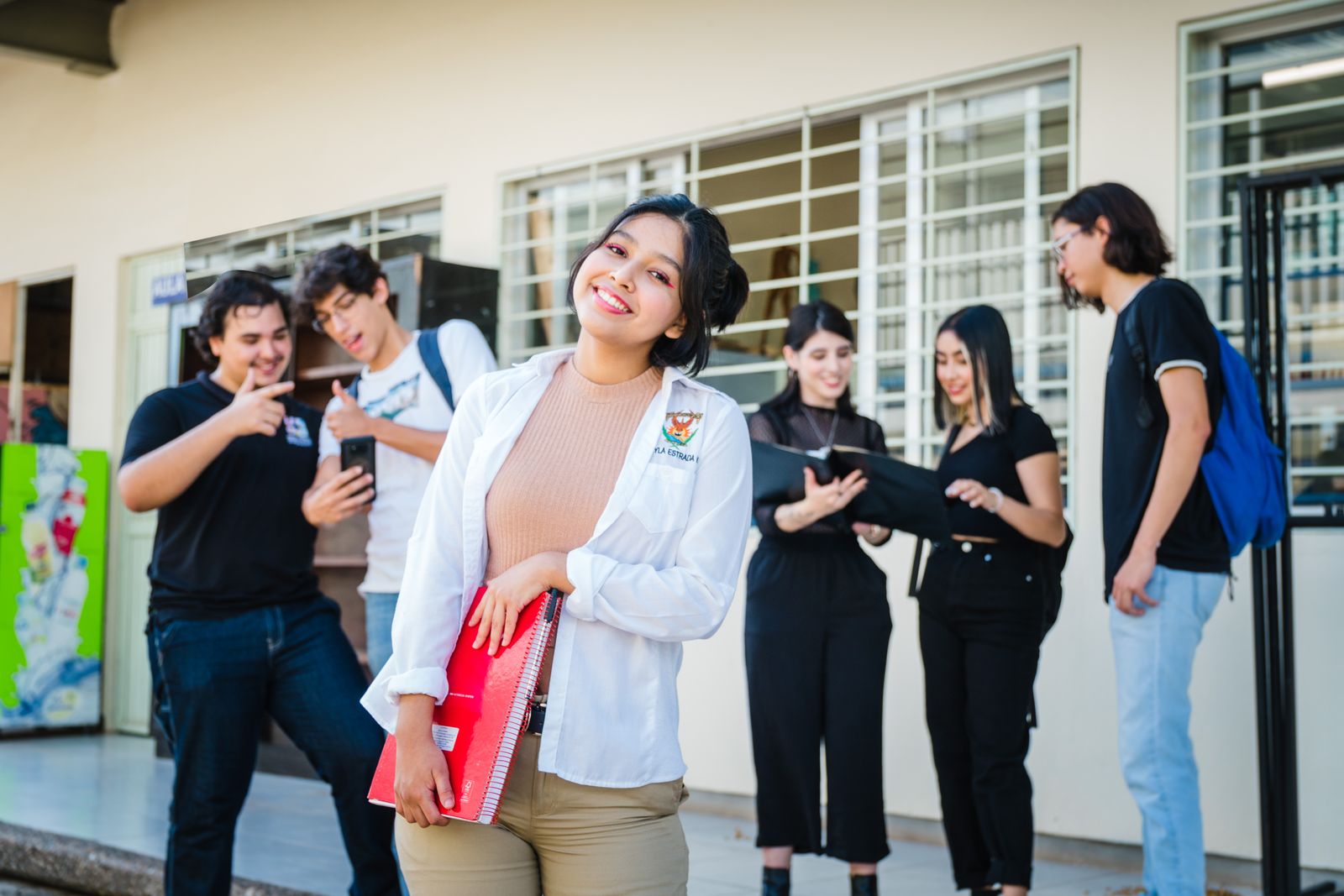 Grupo de estudiantes latinoamericanos sonriendo, con mochilas y cuadernos, en un campus universitario