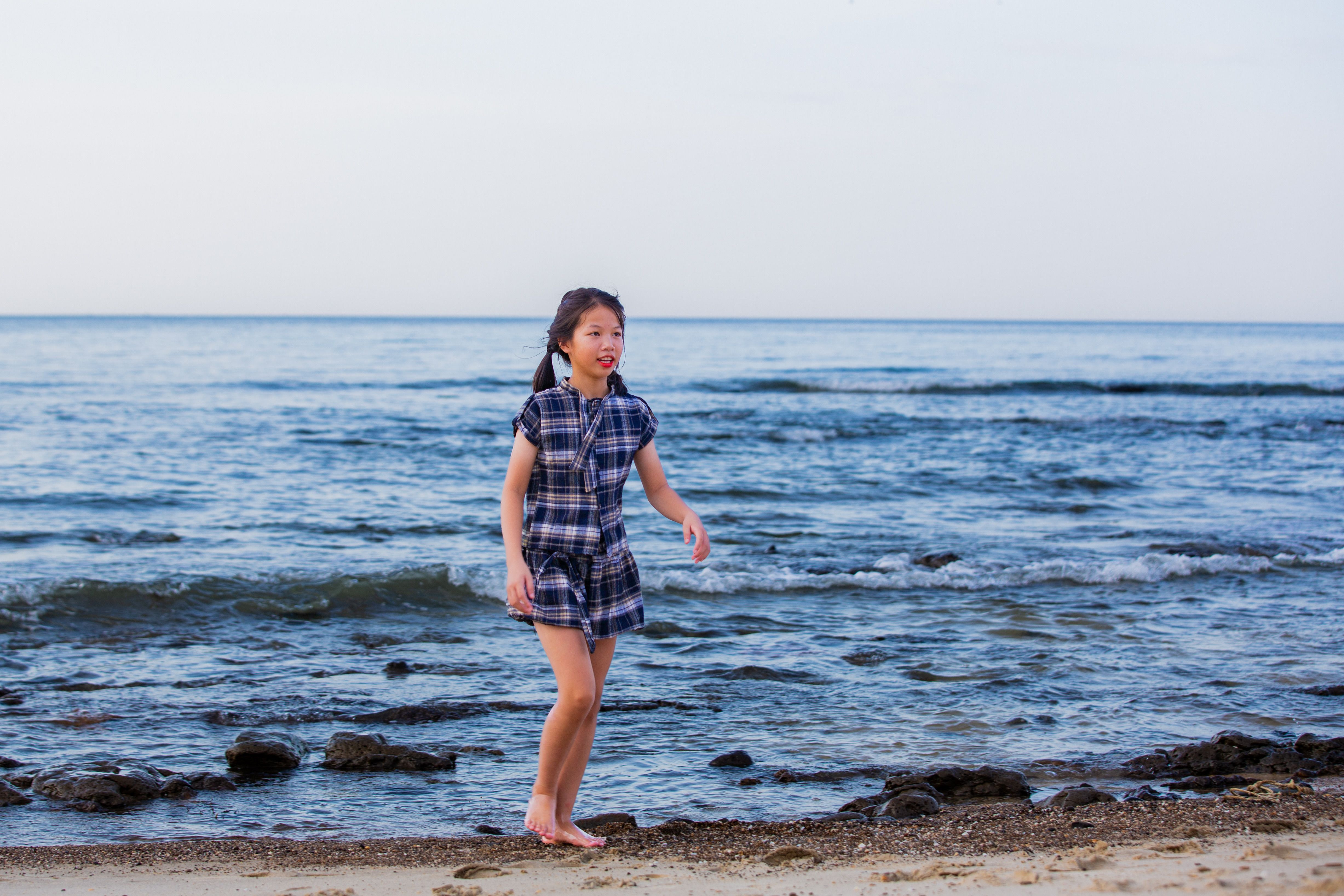 A young girl walking along a beach with the ocean waves in the background.