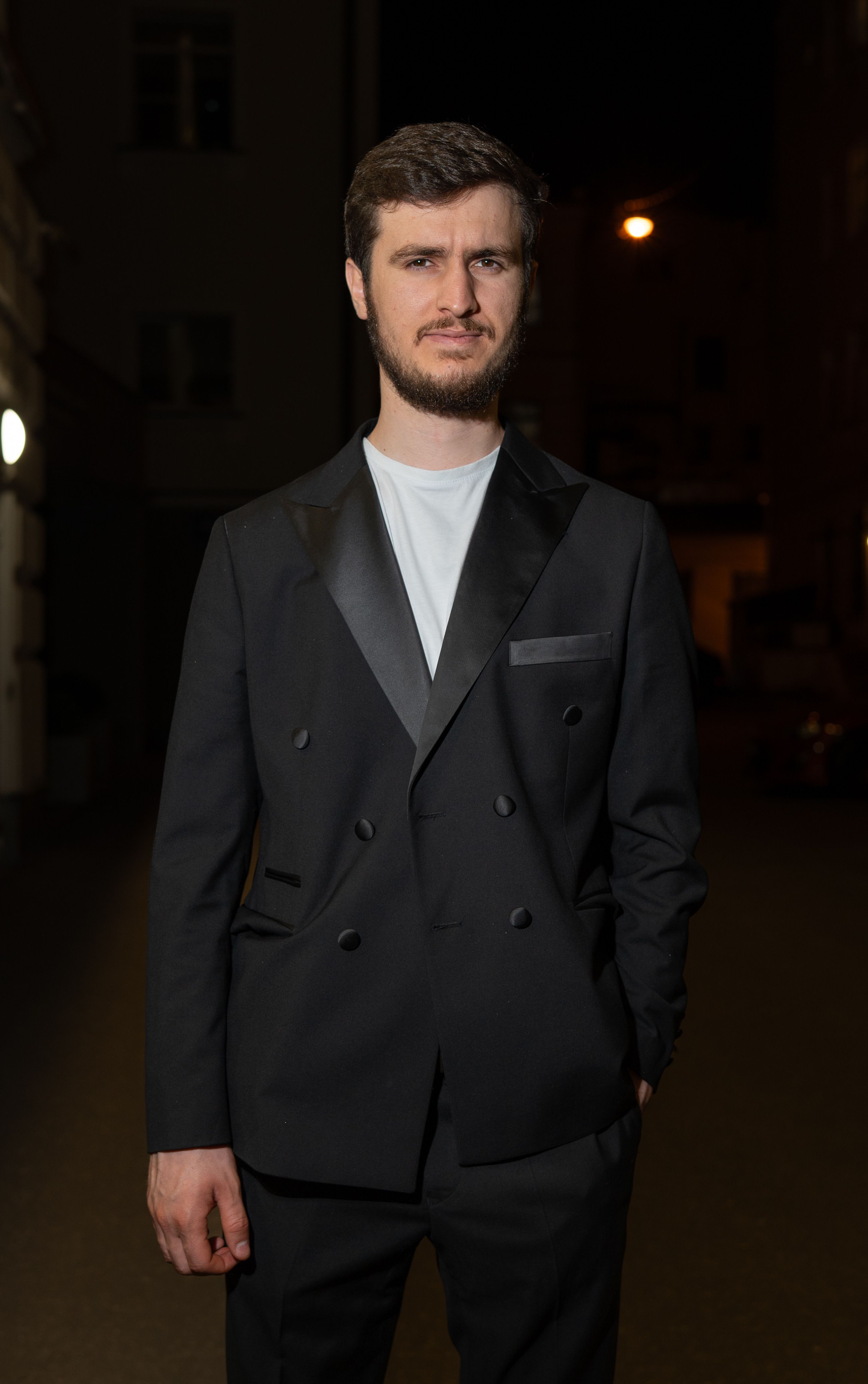 Portrait of a stylish man in a tuxedo standing outdoors at night. Urban setting with dramatic lighting adds sophistication.