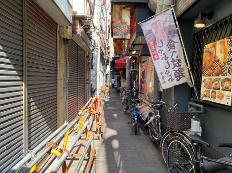 A sunlit narrow alleyway lined with bicycles and storefronts in an urban area.