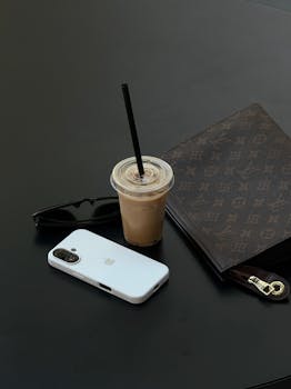 Stylish modern flat lay with iced coffee, smartphone, and designer wallet on a dark surface.