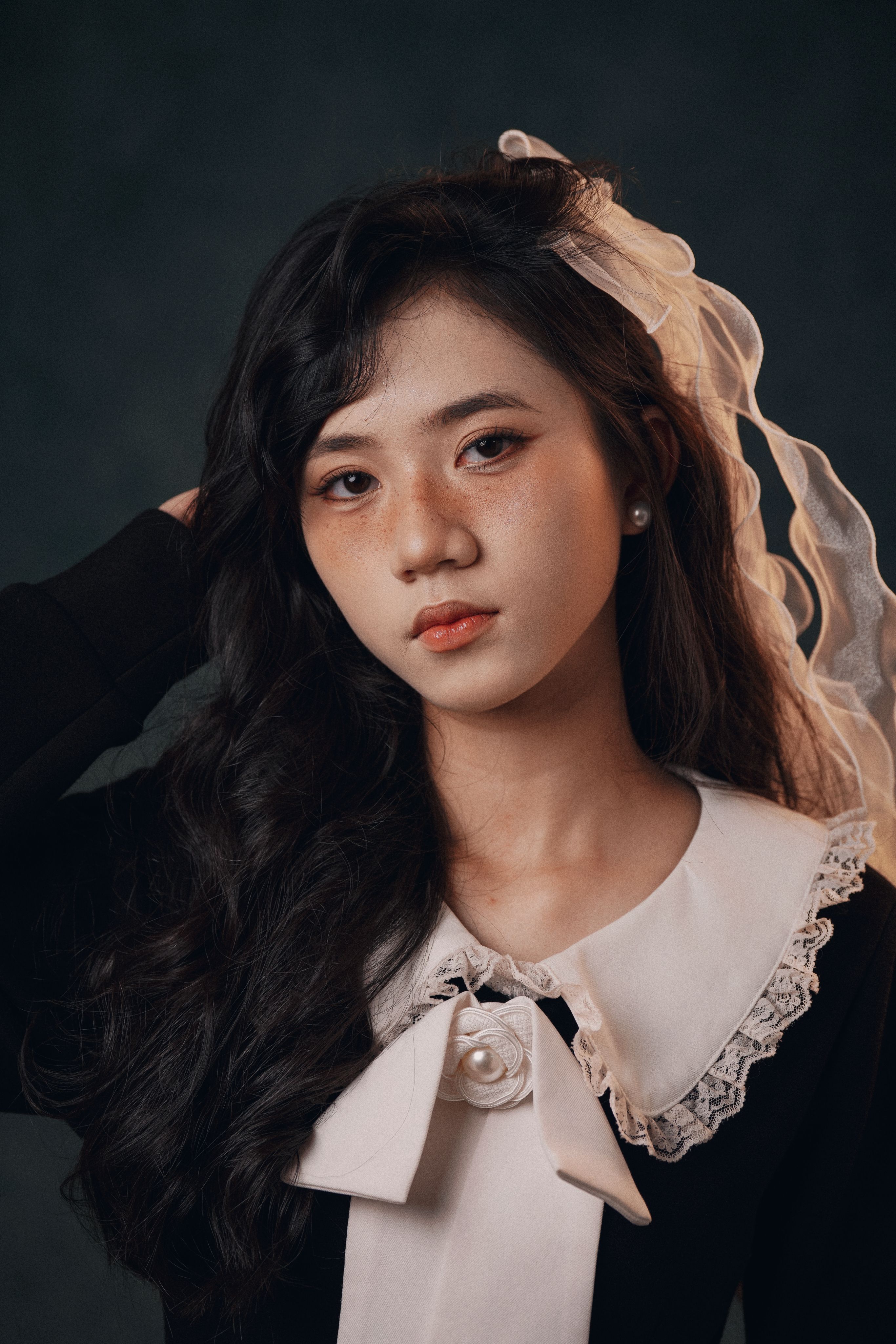 Portrait of a young woman with long hair wearing classic attire and lace headpiece.